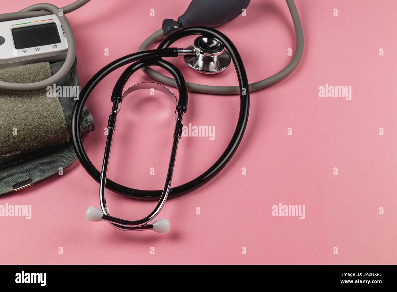 Ein schwarzes Stethoskop und ein Blutdruckmessgerät sind auf einer rosafarbenen Oberfläche abgebildet, die wichtige medizinische Werkzeuge für Gesundheitsüberwachung und -Beurteilung darstellen Stockfoto