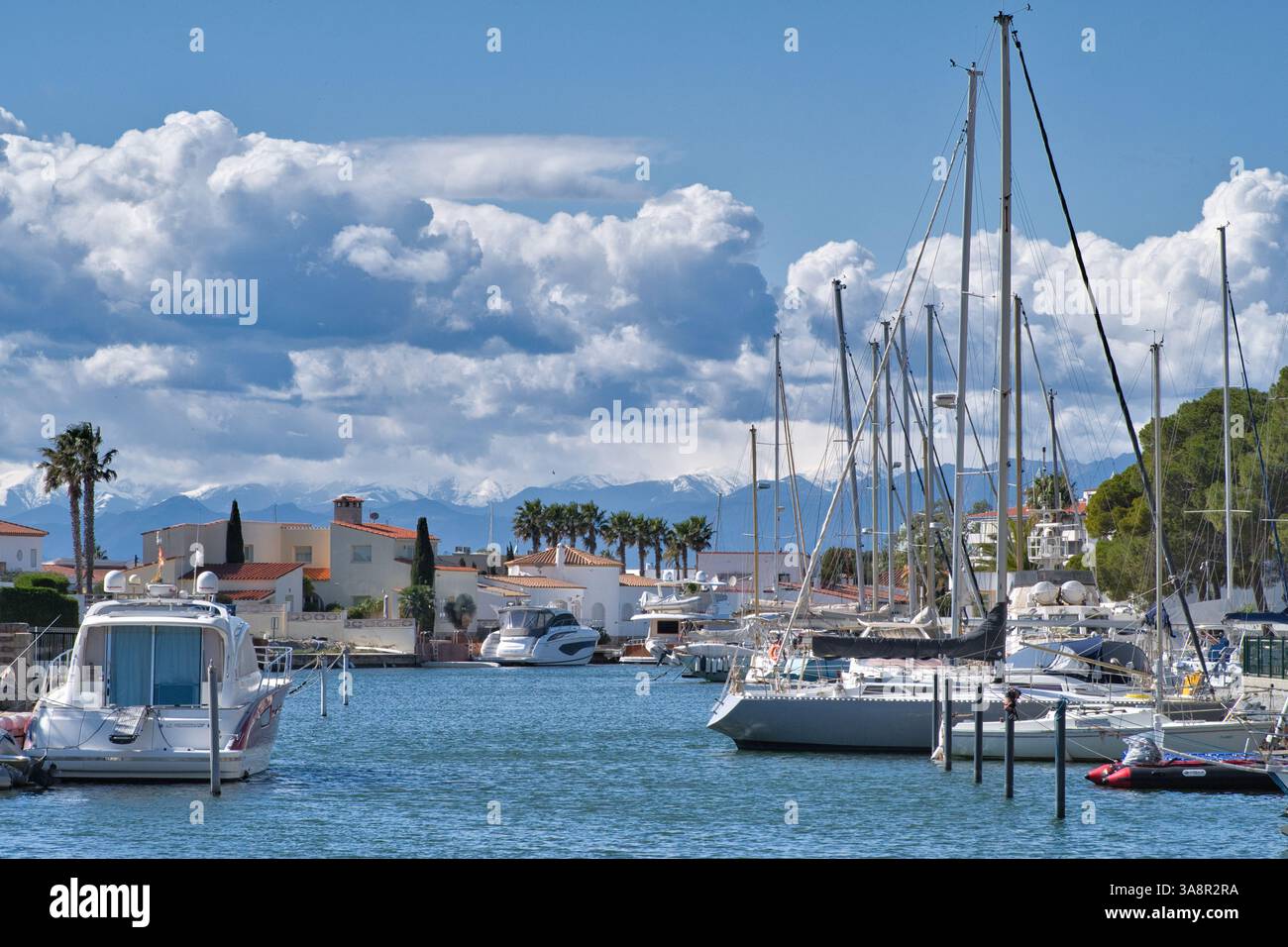 Roses Girona Spanien 20.03.25 helle Sonne über einem Salzwasserwasserweg. Verankerte Yachten und Motorkabinen-Cruiser. Spanische Villen. Terrakottadächer. Schnee Stockfoto