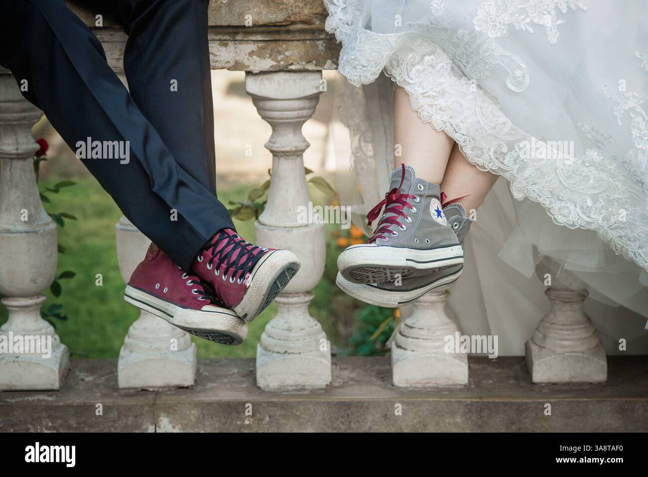 Eine Braut und ein Bräutigam, die auf einem Balkon in einem Park sitzen und Sportschuhe tragen Stockfoto