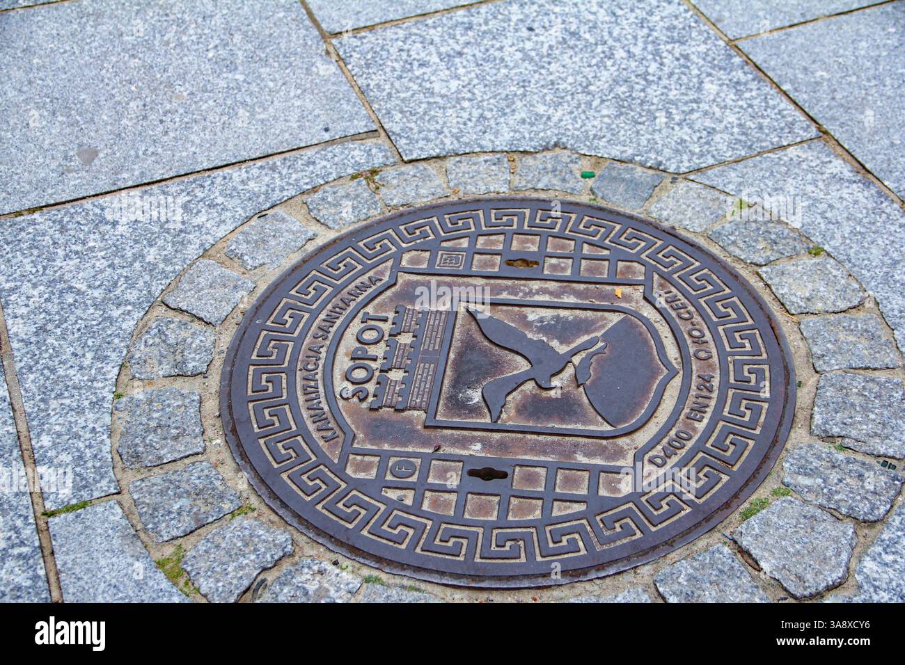 Sopot, Polen - 11.11.2024: Ein Mannlochdeckel mit dem Wappen von Sopot, eingebettet in eine Kopfsteinpflasterstraße. Stockfoto