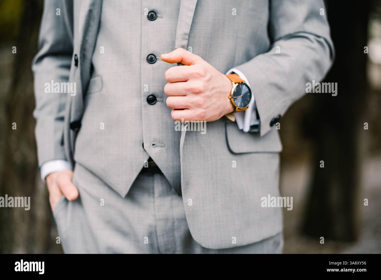 Ein Mann in einem grauen Anzug steht mit einer Hand in der Hosentasche und die andere hält sich am Revers seiner Jacke fest. Abgeschnitten. Gesichtslos Stockfoto