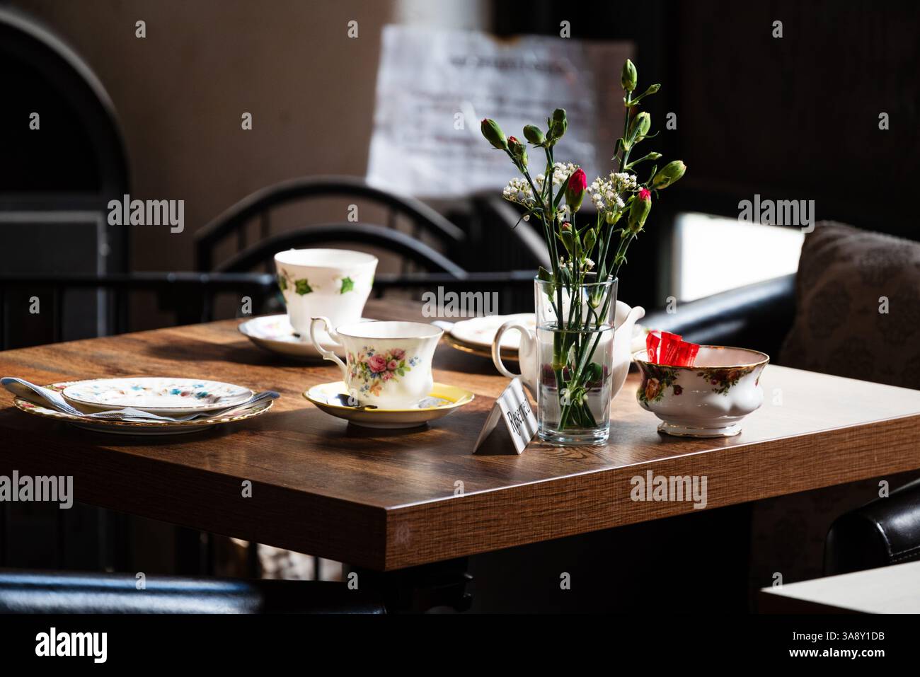 Ein reservierter Tisch für den Nachmittagstee mit zartem blumenpüree, einer kleinen Vase mit Blumen und Zuckerpackungen wartet auf die Gäste Stockfoto