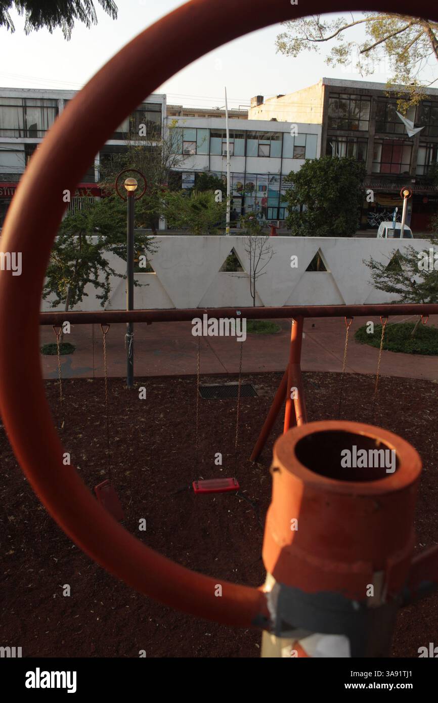 Traumhafte Golden Hour in Guadalajara: Schaukeln des Parks, eingerahmt durch eine gebrochene kreisförmige Linse – surreales Morgenlicht, überwachsene Natur und urbaner Verfall Stockfoto