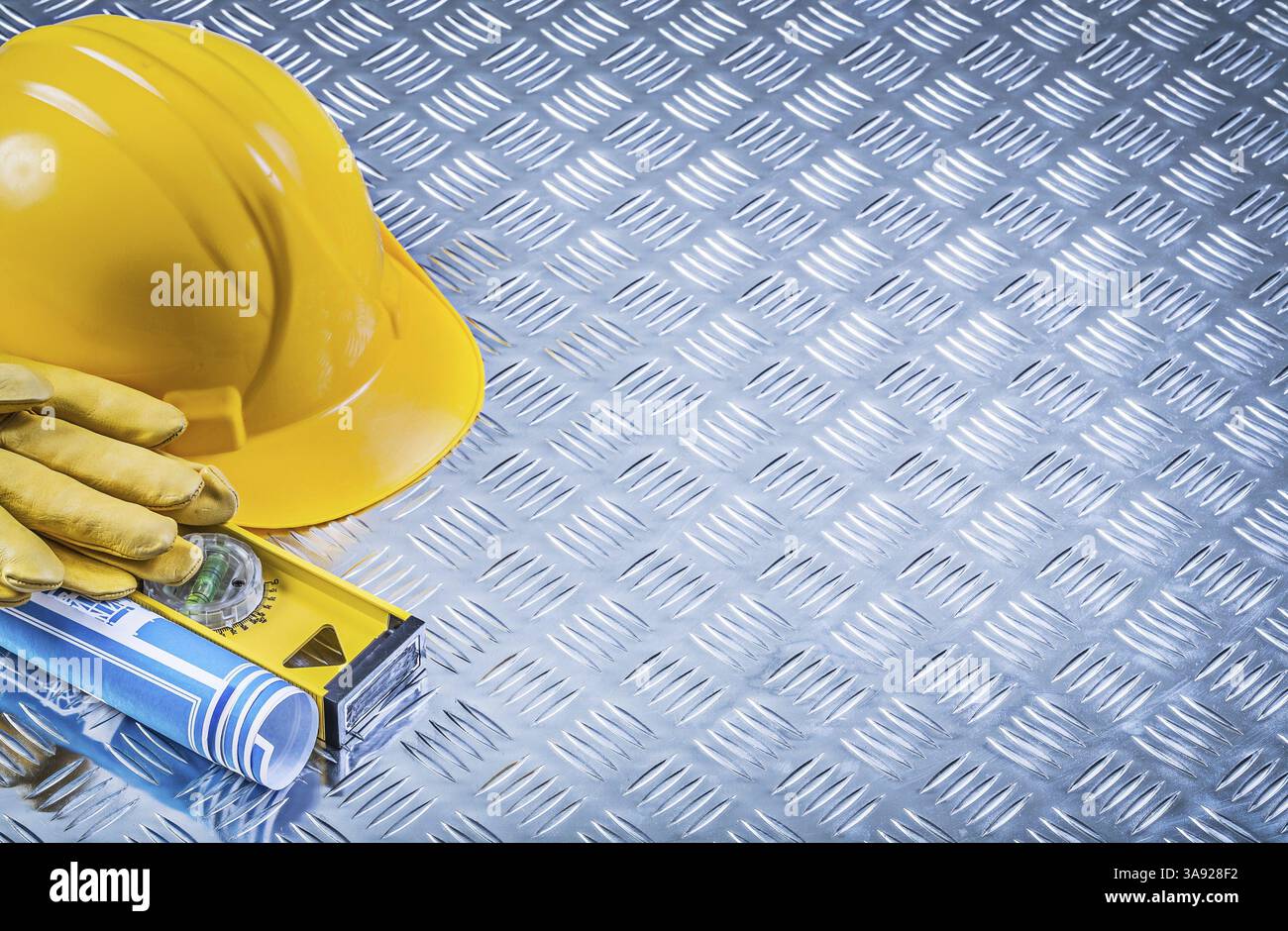 Zusammensetzung der blau gerollten Blaupausen des Bauhelms Sicherheitshandschuhe Konstruktionsebene auf gerilltem Metallhintergrund Stockfoto