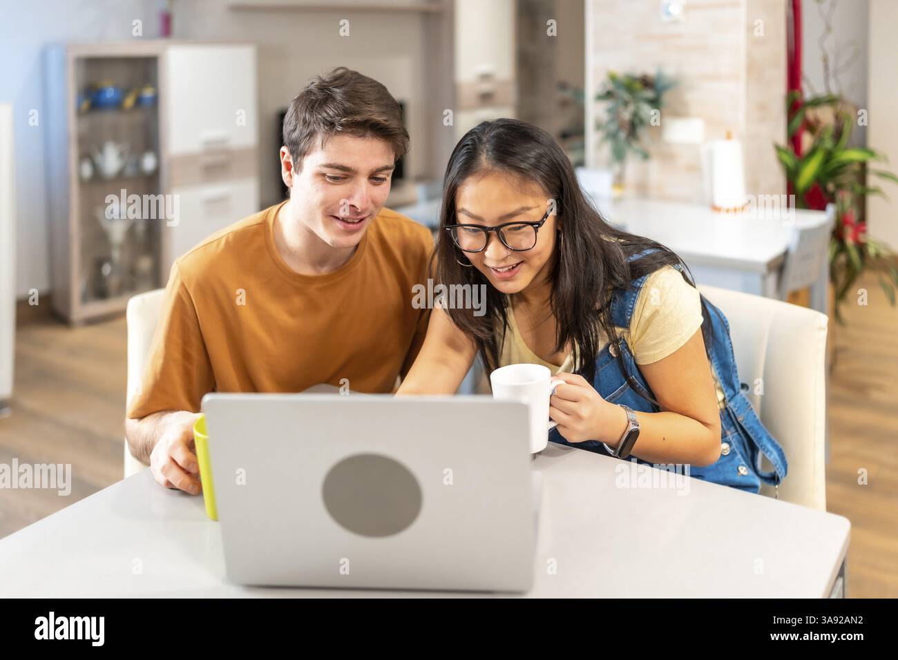 Ein multiethnisches Paar, das einen Laptop nutzt und zu Hause Kaffee trinkt, genießt einen entspannenden Moment zusammen Stockfoto