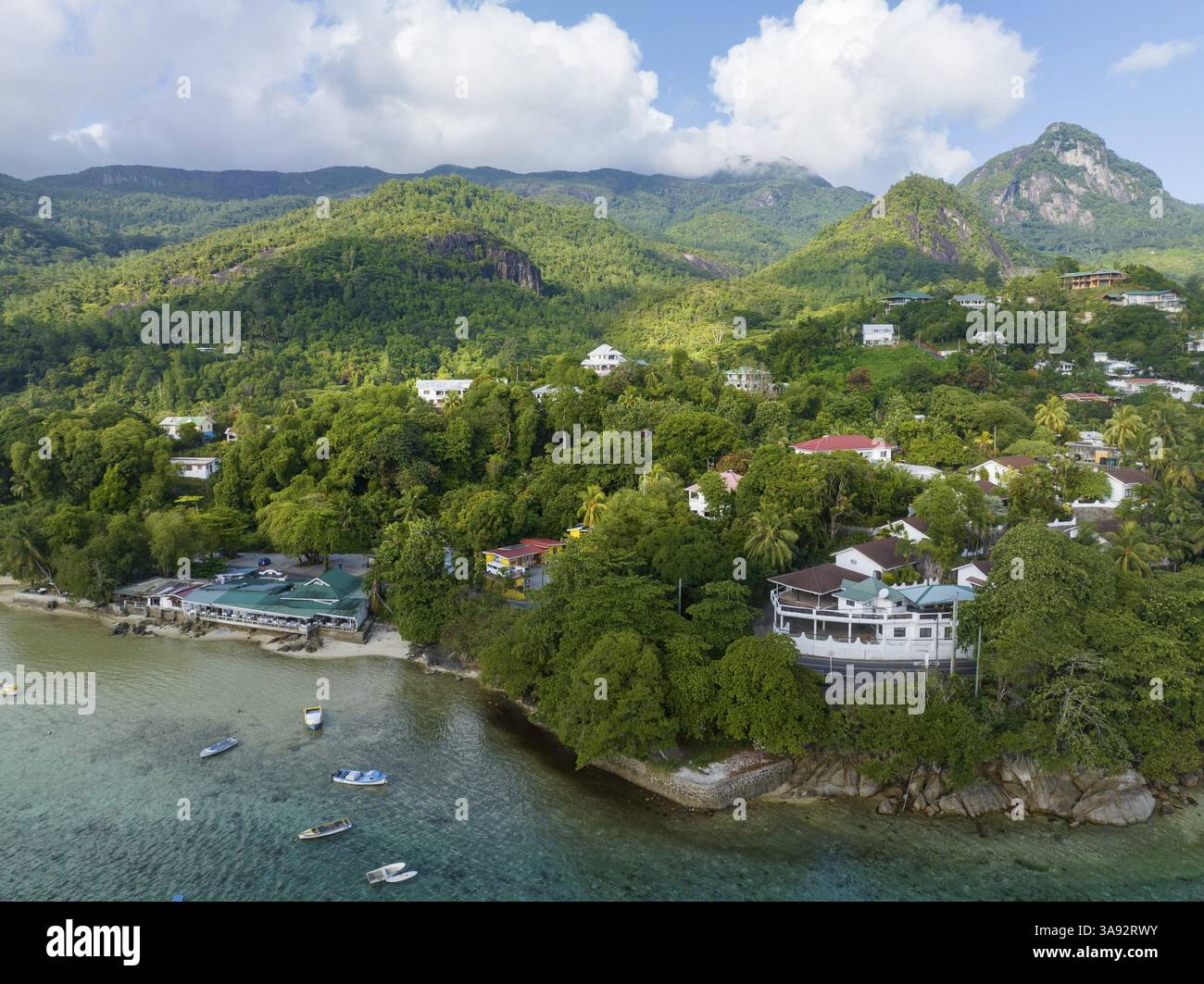 Dorf an einer Küste, umgeben von grünen Hügeln und tropischer Vegetation unter einem leicht bewölkten Himmel, SEYCHELLEN, Port Glaud Stockfoto