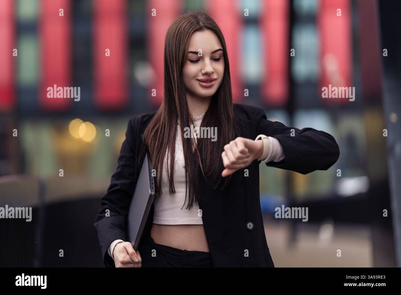 Die Kraft bewegt sich, die Zeit wird getickt. Eine Geschäftsfrau läuft in der Abenddämmerung durch die Stadt, mit Laptop in der Hand, überprüft ihre Armbanduhr. Der Rhythmus des Ehrgeizes trifft auf den Stockfoto