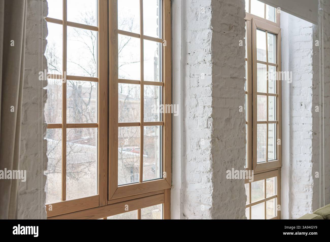 Große Fenster mit Holzrahmen im Loftinern mit weißen Ziegelwänden in einem modernen Apartment oder Haus. Innenausstattung, Architekturelement, urba Stockfoto