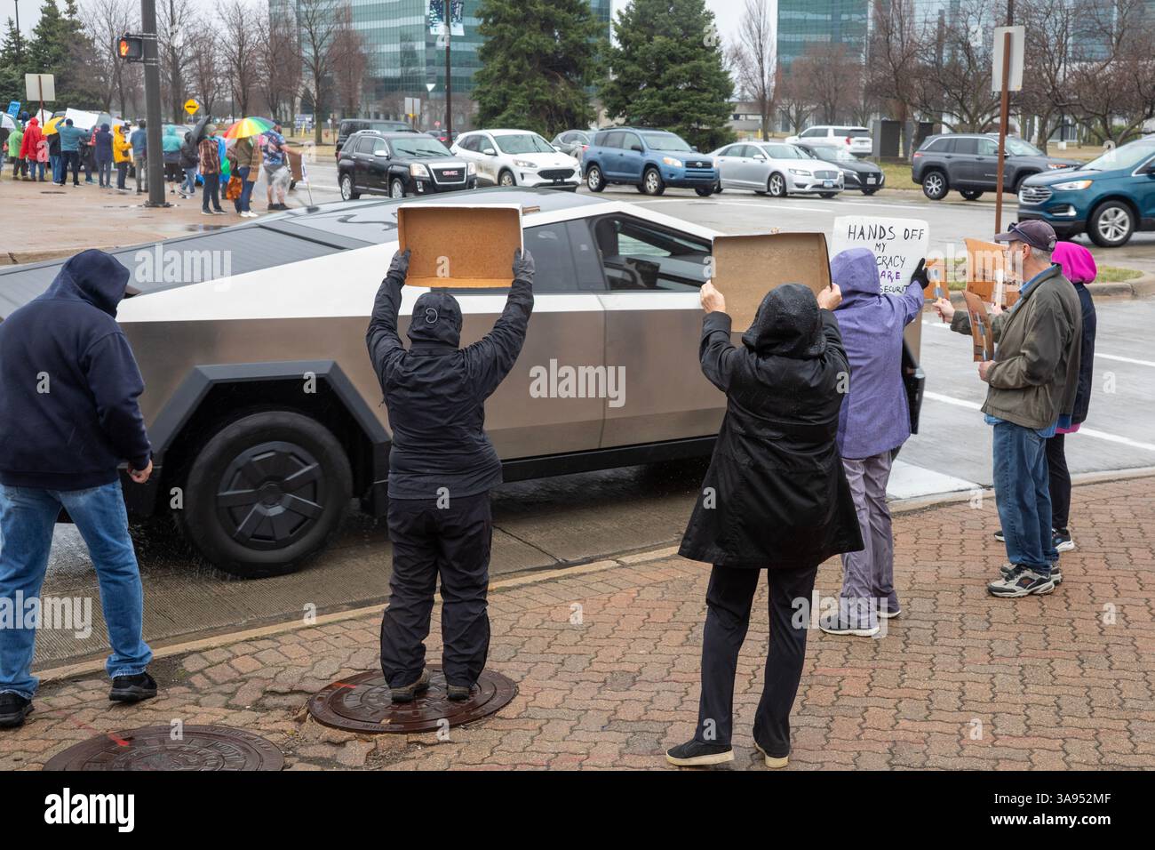 Troy, Michigan, USA. März 2025. Ein Tesla Cybertruck fährt vorbei, als sich die Leute im Regen vor dem Tesla Showroom in der Somerset Mall versammelten, um gegen die Rolle des Tesla-Besitzers Elon Musk bei der Zerschlagung der Regierungsdienste zu protestieren. Es war eine von vielen „Tesla Takedown“-Aktionen, die im ganzen Land und im Ausland geplant waren. Quelle: Jim West/Alamy Live News Stockfoto