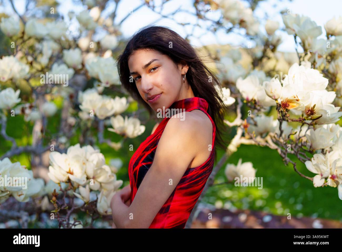 Eine Frau in einem atemberaubenden roten Kleid genießt einen schönen Frühlingstag umgeben von blühenden Magnolienblüten Stockfoto