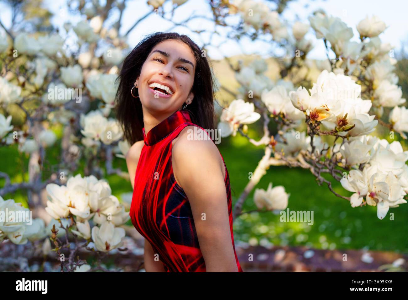 Eine Frau in einem atemberaubenden roten Kleid genießt einen schönen Frühlingstag umgeben von blühenden Magnolienblüten Stockfoto