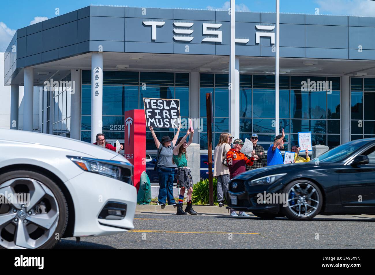 Ein Demonstrant hält ein TeslaFire Musk-Schild, während der Verkehr während eines wöchentlichen Protestes vor dem Tesla-Händlerbetrieb am Arden Way vorbeigeht. Stockfoto