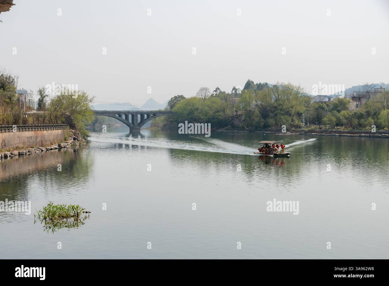 Traditionelles chinesisches Boot, das durch den Misty Mountain River gleitet – eine ruhige Fahrt auf dem Wasserweg in üppiger grüner Landschaft Stockfoto