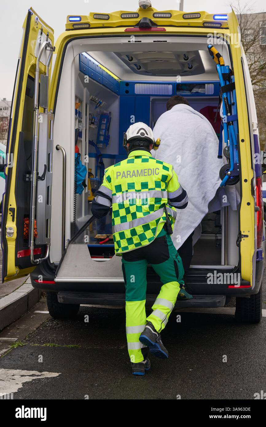 27.03.2025, Sanitäter in gut sichtbarer Uniform und Helm hilft einem Patienten, in einen Krankenwagen zu gelangen. Der Patient ist in eine weiße Decke eingewickelt, Indicatin Stockfoto