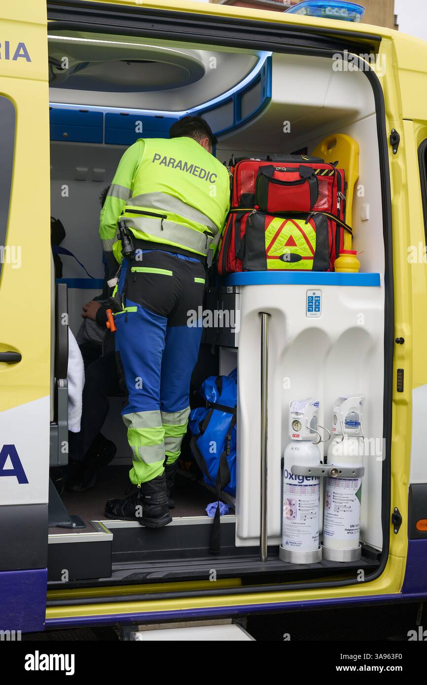 Nahaufnahme eines gelben Notarztwagens mit offener Seitentür, in dem medizinische Geräte und Sauerstofftanks zu sehen sind. Ein Sanitäter, der einen High-VI trägt Stockfoto