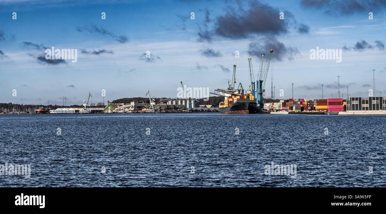 Blick auf einen belebten Seehafen mit Frachtcontainern, Kränen und einem Schiff an einem sonnigen Tag. Stockfoto