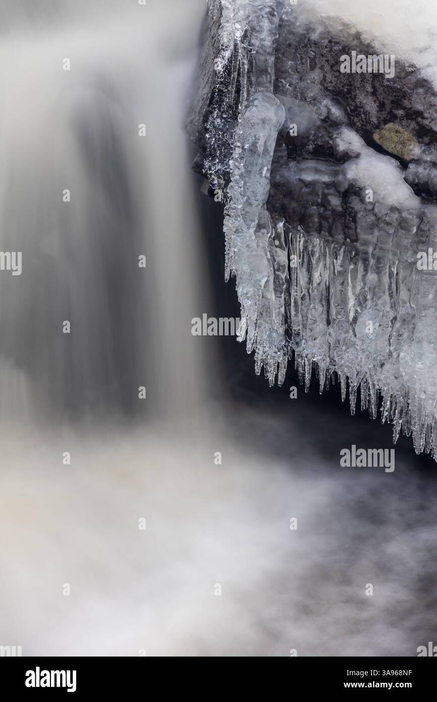 Nahaufnahme eines gefrorenen Wasserfalls mit nebligem fließendem Wasser, kurzen Eiszapfen, die von Felsen hängen, und Eisformationen, die die Steinoberfläche bedecken Stockfoto