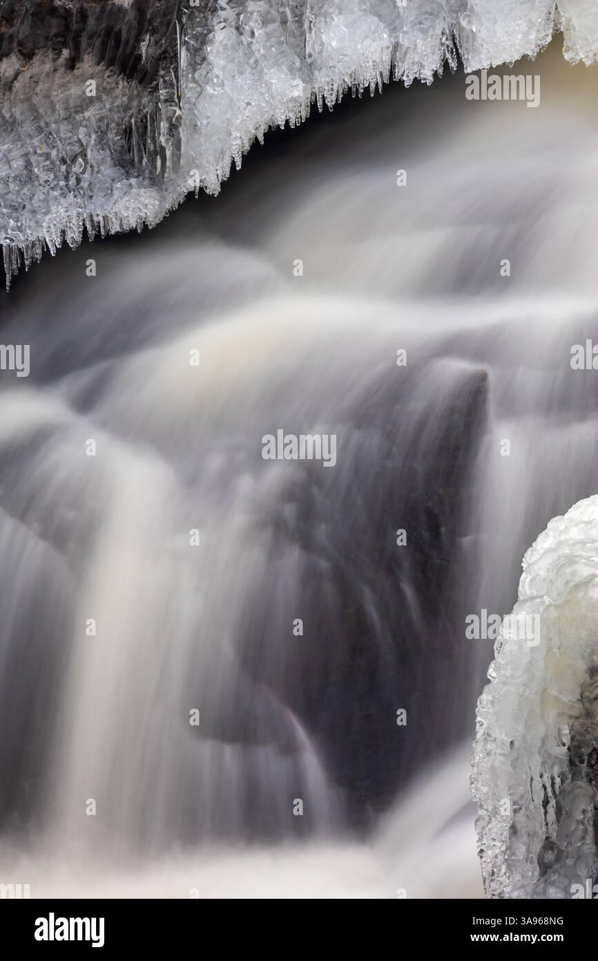 Nahaufnahme eines gefrorenen Wasserfalls mit nebligem fließendem Wasser, kurzen Eiszapfen, die von Felsen hängen, und Eisformationen, die die Steinoberfläche bedecken Stockfoto