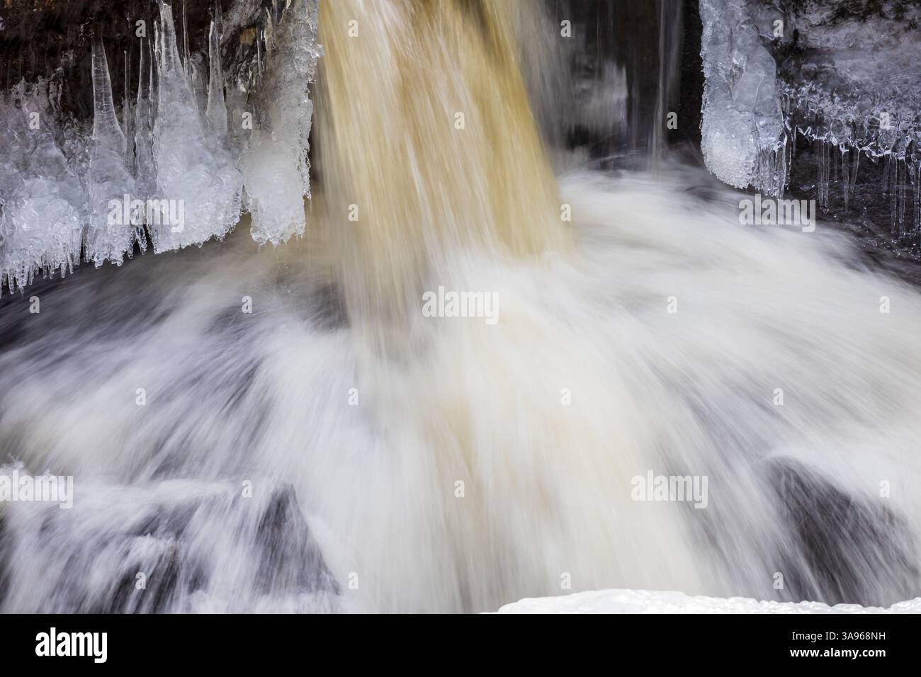Nahaufnahme eines gefrorenen Wasserfalls mit nebligem fließendem Wasser, kurzen Eiszapfen, die von Felsen hängen, und Eisformationen, die die Steinoberfläche bedecken Stockfoto
