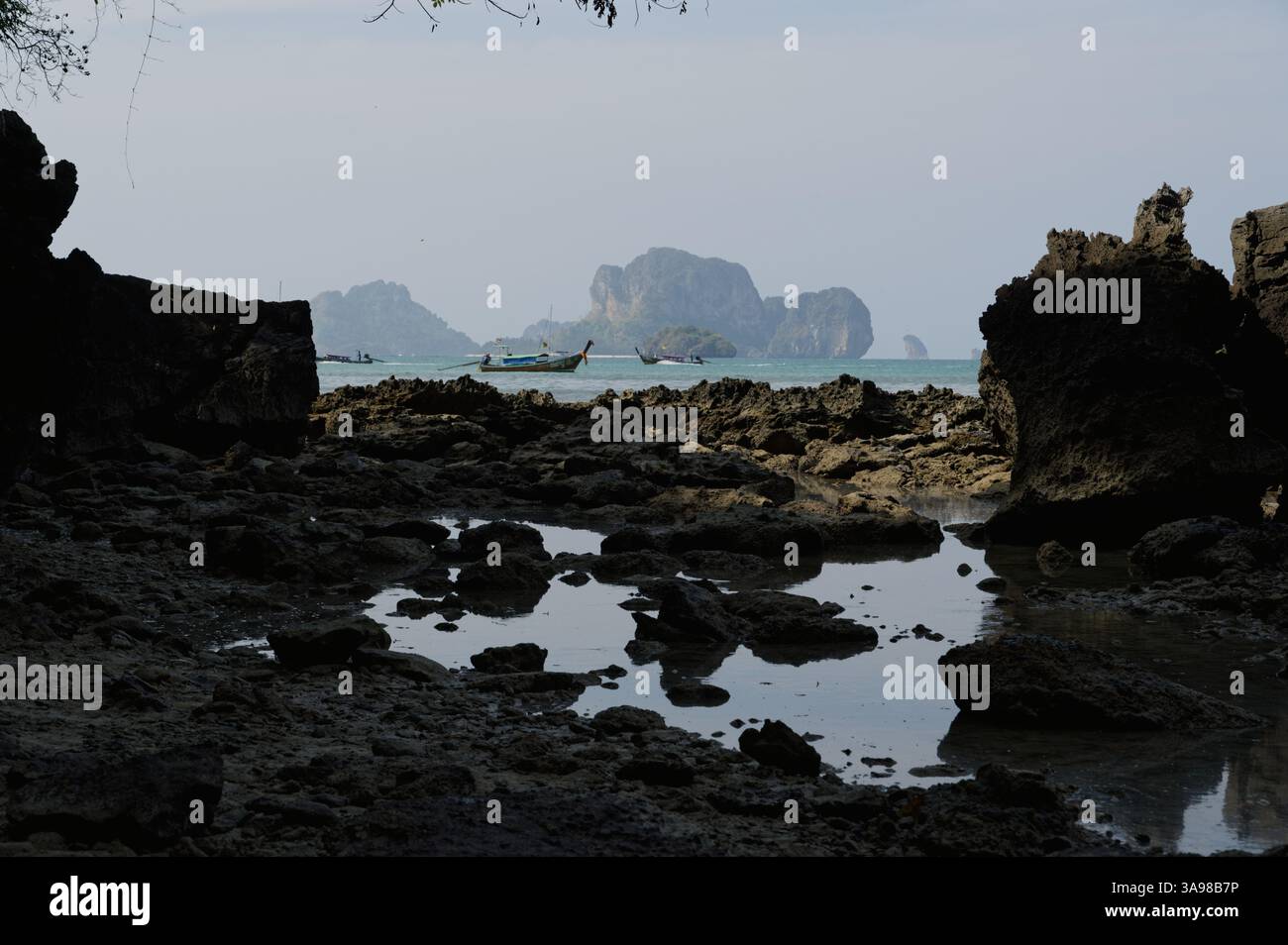Langboot-Boote gleiten an Kalksteininseln vorbei, während das Morgenlicht bei Ebbe auf Felsbrocken trifft Stockfoto