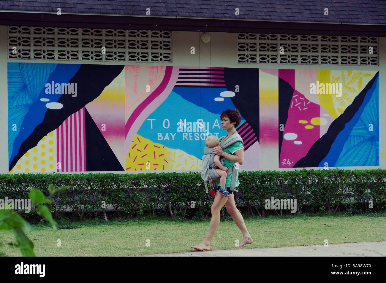 Mutter und Kind schlendern vorbei an dem lebhaften Wandgemälde des Tonsai Bay Resort Stockfoto