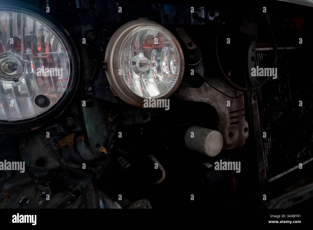 Vorderansicht eines Fahrzeugs in einer Werkstatt mit ausgebautem Stoßfänger und Kühlergrill, wobei zwei kreisförmige Scheinwerfer und ein Kühler freigelegt werden. Stockfoto