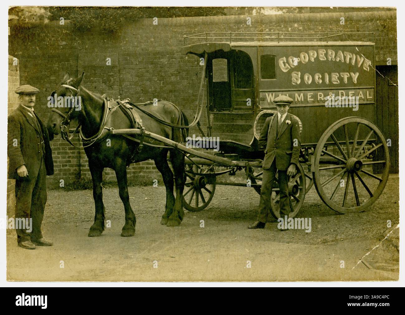 Original-Postkarte aus der Zeit des 1. Weltkriegs mit einem Mann aus der Arbeiterklasse und seinem Lehrjungen, der neben einem Lieferwagen für Pferdewagen, einem Vintage-Pferd und einem Wagen steht. Viktorianischer Pferdewagen. Cooperative Society (The Co-op), Walmer & Deal (Region) Werbeschilder auf der Seite. Walmer / Deal in Kent, England, Großbritannien um 1914 Stockfoto