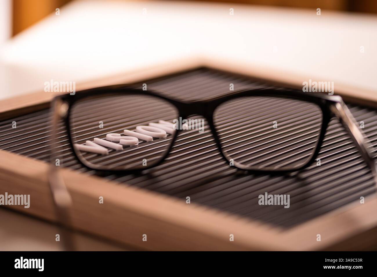Auf einer Oberfläche aufliegende Brillen mit dem Wort „Vision“ auf einer Tafel, was die Klarheit und das Konzept der Sehkorrektur unterstreicht Stockfoto