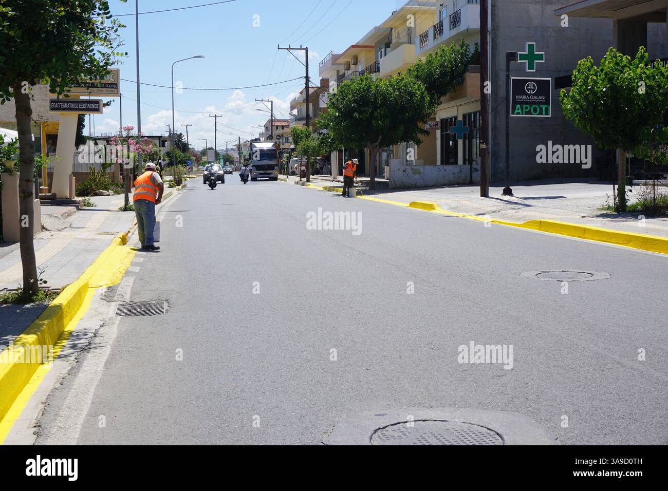 Zwei Arbeiter in fluoreszierenden Westen halten Pinsel und lackieren die Bordsteinkanten mit gelber Farbe auf einer Straße Stockfoto