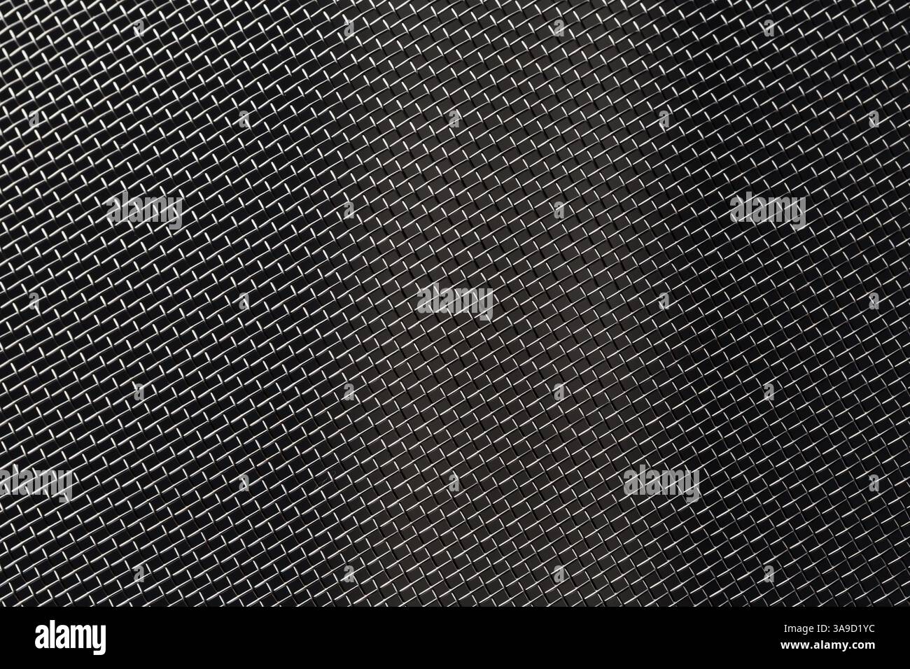 Feines Metallgeflecht auf dunklem Hintergrund, schräg angelegt und seitlich beleuchtet. Stockfoto