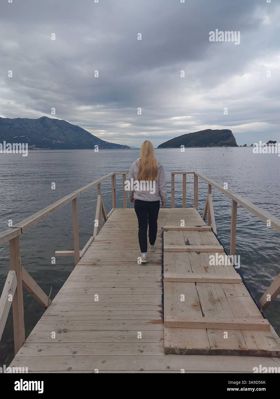 Frau, die auf einem hölzernen Pier in Richtung Meer geht – ruhige Reiseszene Stockfoto