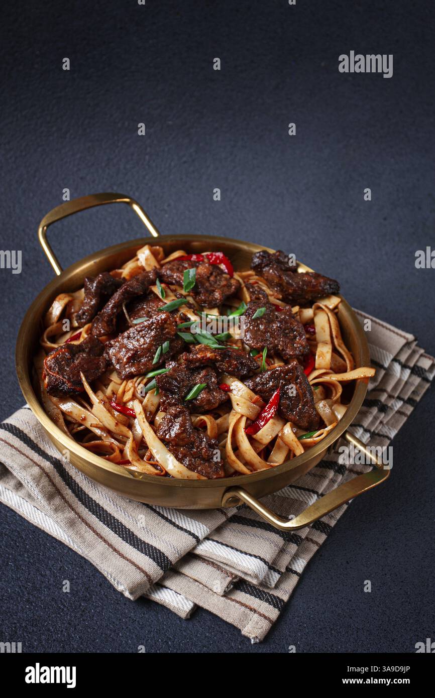 Udon-Nudeln mit mongolischem Rindfleisch, grünen Zwiebeln und Gemüse, in einer Messingpfanne, auf grauem Hintergrund, hausgemacht, keine Leute Stockfoto
