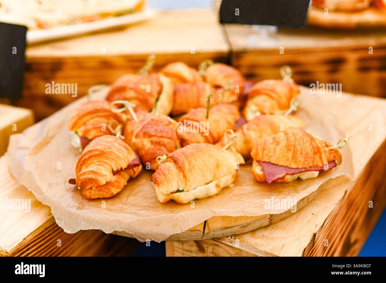 Nahaufnahme von frisch zubereiteten Mini-Croissant-Sandwiches gefüllt mit Feinkostfleisch und Gemüse, auf Pergament für Catering-Service. Stockfoto