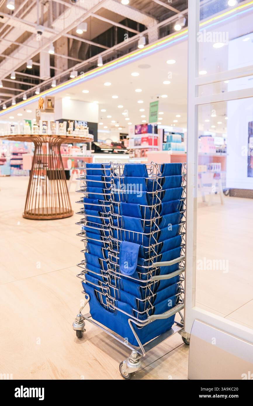 Ein blauer Einkaufswagen, gefüllt mit blauen Einkaufstaschen, wird in einem Geschäft geparkt. Der Wagen ist voll mit verschiedenen Arten von Taschen, einschließlich Handtaschen, Rucksäcken, und Stockfoto
