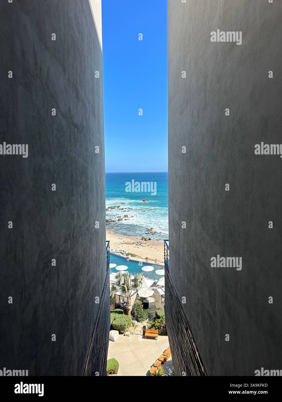 Ein atemberaubender Blick auf das Meer, eingerahmt zwischen zwei modernen Gebäuden, mit Blick auf einen luxuriösen Resortpool und Sandstrand mit Sonnenschirmen. - Smartphone-aufgenommenes Stockfoto