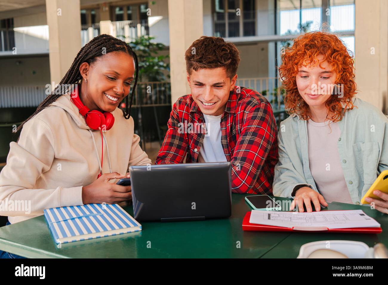 Ein dynamisches Trio motivierter Studenten, die gemeinsam auf einem Laptop arbeiten, Wissen und Erkenntnisse austauschen, während sie die Gesellschaft des anderen genießen und in einer akademischen Umgebung voller Begeisterung Teamarbeit fördern Stockfoto