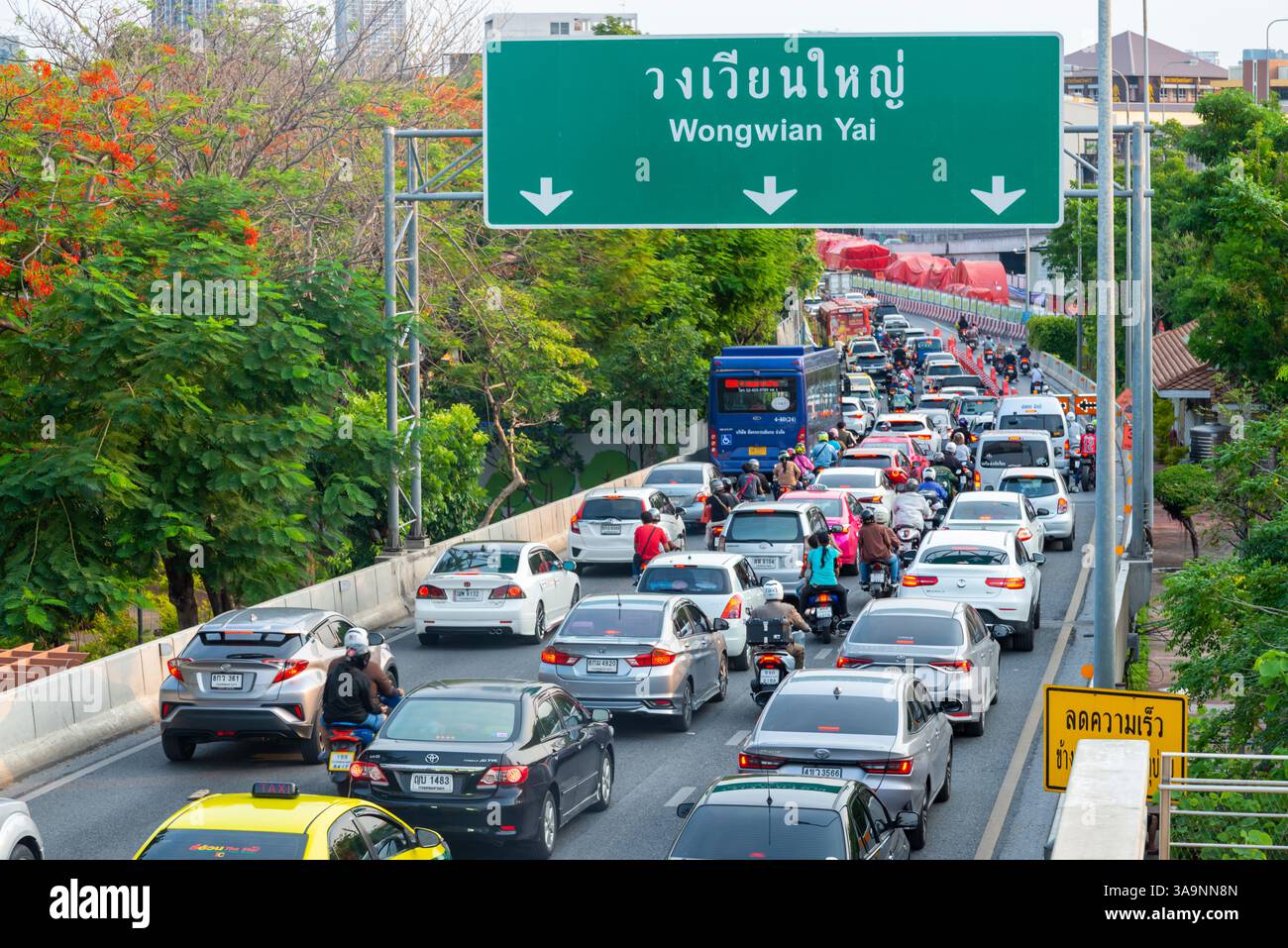 Thailand-15 Mai 2024: Warteschlangen mit viel Verkehr am Nachmittag bewegen sich langsam unter dem umweltfreundlichen erhöhten Weg, gefüllt mit Pflanzen, Blumen, Grün Stockfoto