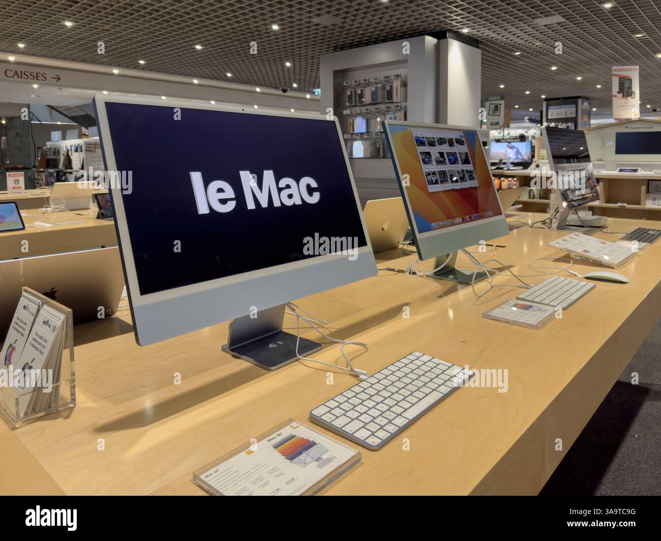 Paris, Frankreich - 3. Oktober 2023: IMac-Desktop-Modelle mit Tastaturen und Display-Bildschirmen sind auf Holztischen unter Deckenleuchten im A ordentlich angeordnet Stockfoto