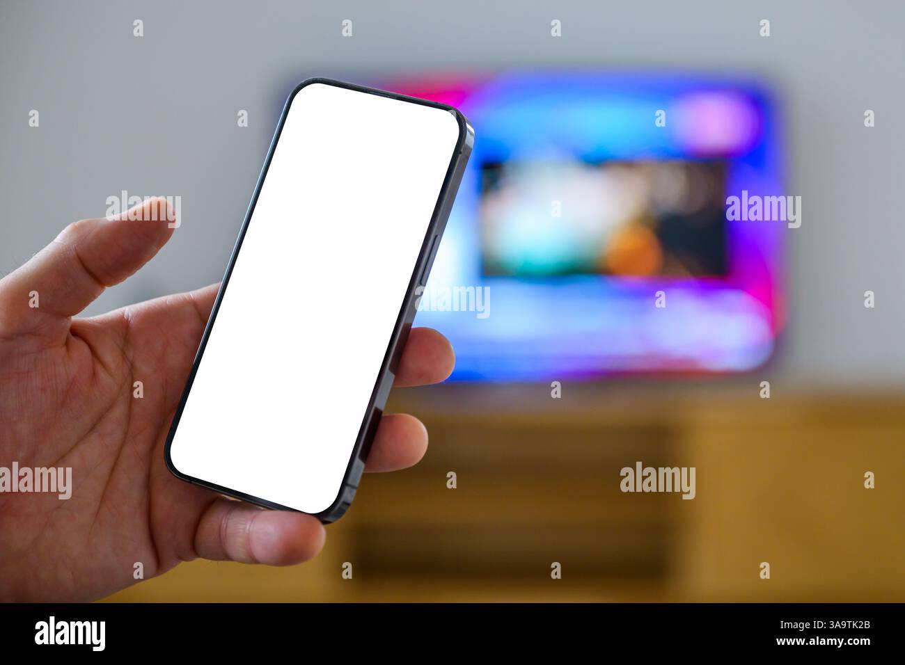 Smartphone-Mockup-Bildschirm, Mann, der das Handy vor dem Fernseher hält, tv-App und tv-Programm-Auflistung Konzept, selektiver Fokus Stockfoto