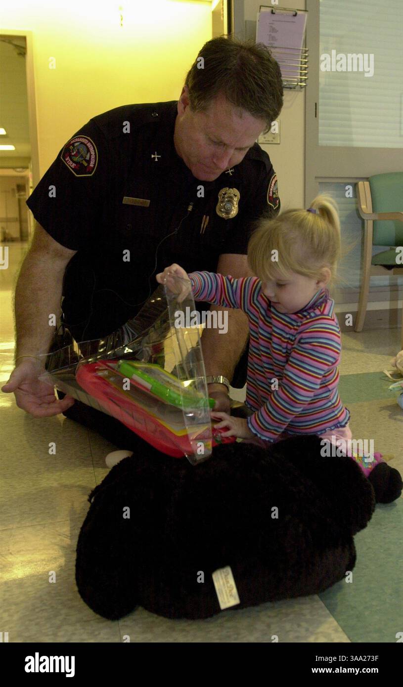Tom Perkins von Sacramento Metropolitan Fire überreicht Madison Phelps (cq), 2, im UC Davis Children's Hospital, 4. Dezember 2003, ein neues Spielzeug. Sacramento Bee/ Florence Low /ZUMA Press Stockfoto