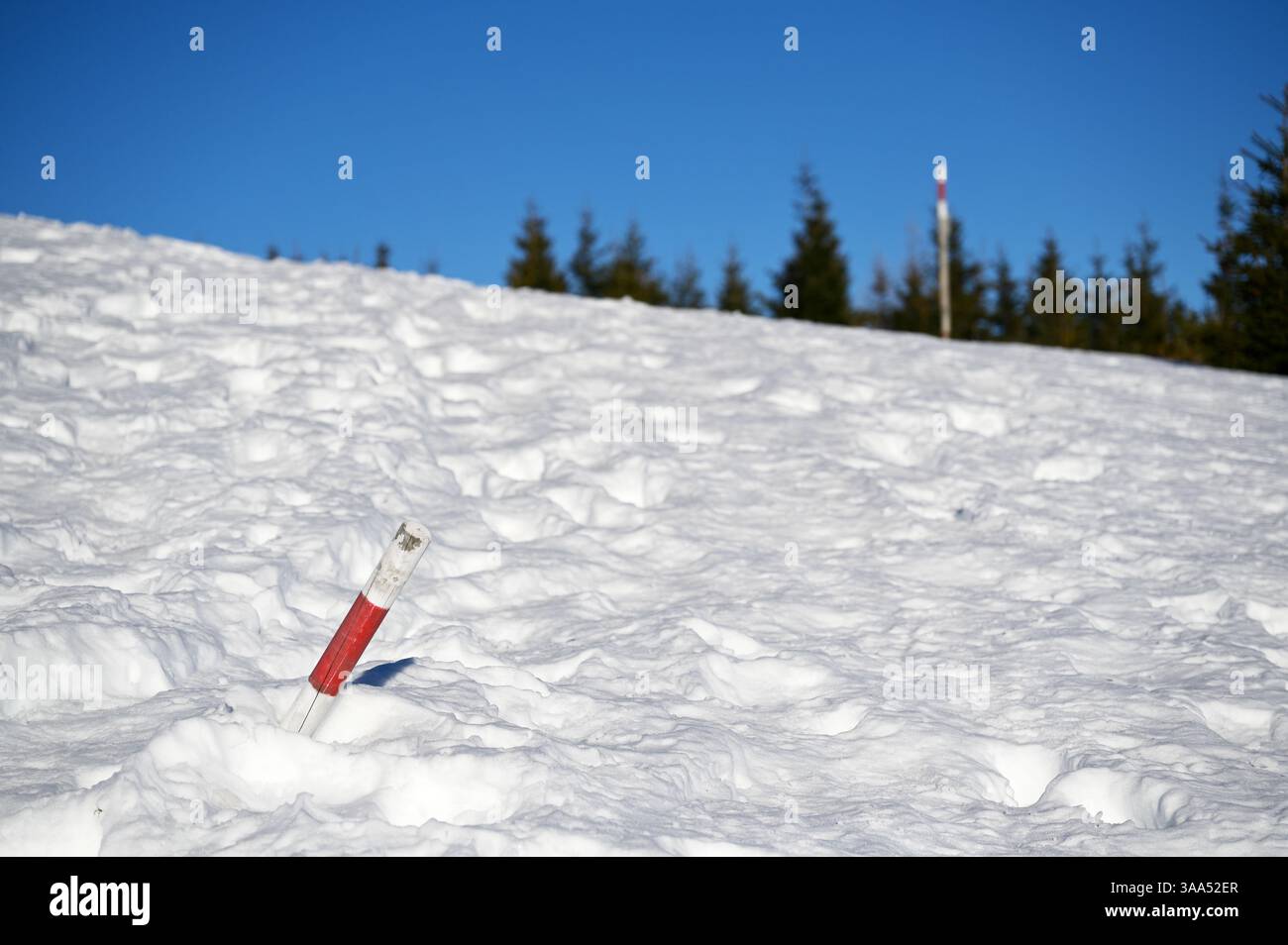 Wegmarkierung, die durch die Winterschneelandschaft führt. Rot-weiße Wegmarkierung, die durch ein verschneite Berggelände führt. Stockfoto
