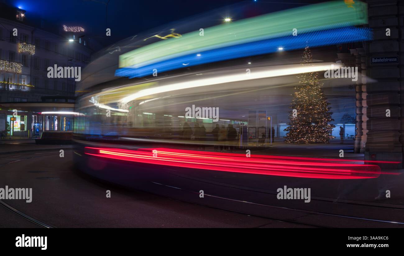 Zürich, Schweiz - 29. Dezember 2024: Eine Langzeitaufnahme einer Straßenbahn, die nachts an einem geschmückten Weihnachtsbaum vorbeifährt und Lichtspuren erzeugt. Parade Stockfoto Zürich, Schweiz - 29. Dezember 2024: Eine Langzeitaufnahme einer Straßenbahn, die nachts an einem geschmückten Weihnachtsbaum vorbeifährt und Lichtspuren erzeugt. Parade Stockfoto