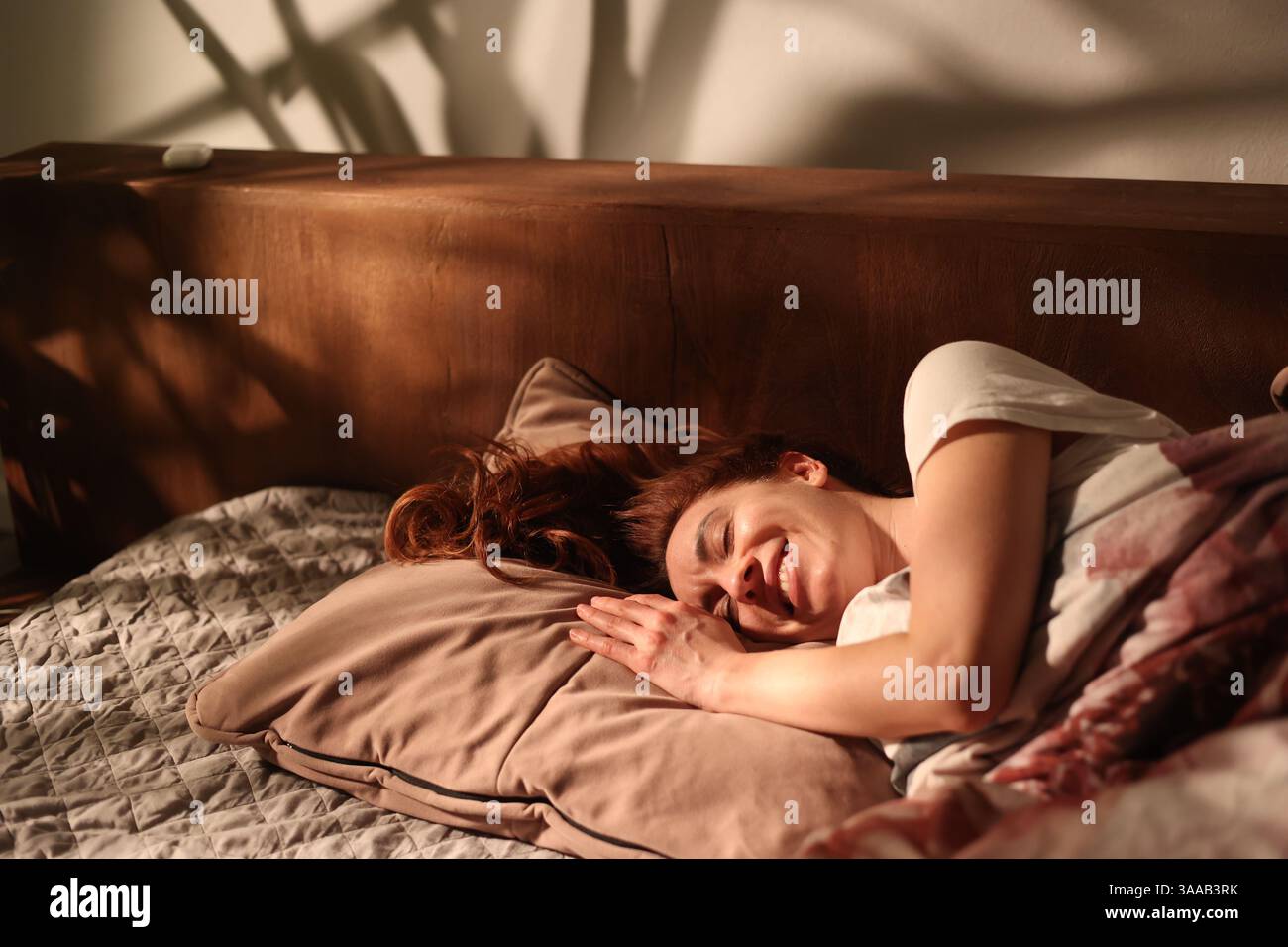 Wunderschönes glückliches Mädchen am Morgen lächelnd im Bett auf Kissen, wunderschönes Licht mit Schatten von Palmen, filmisches Bild unbeschwert glückliches Leben, ECO-f Stockfoto