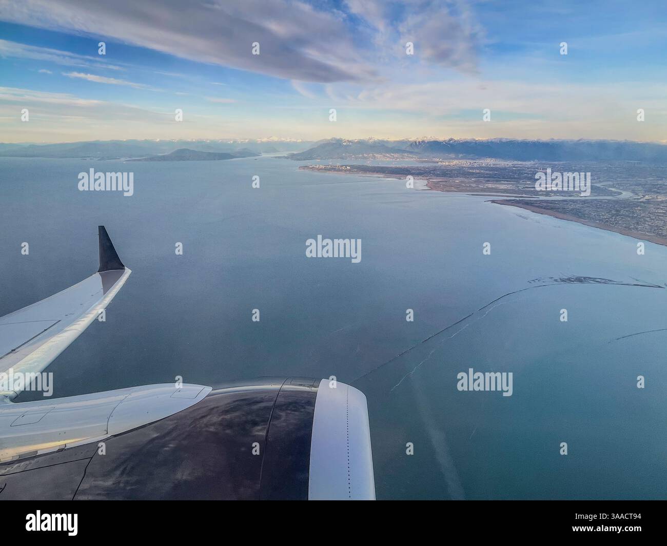Luftaufnahme der Küste und der fernen Berge vom Flugzeugfenster aus mit sichtbarem Flügel, aufgenommen während des Tagesflugs. - Smartphone-aufgenommenes Stockfoto
