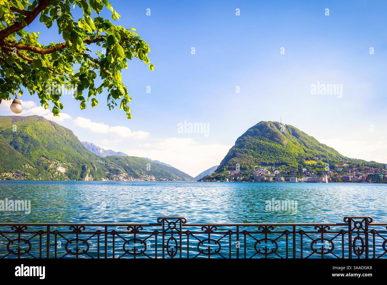 Terrasse und Baum am Luganer See mit Bergen im Hintergrund. Lugano, Kanton Tessin, Schweiz oder Schweizerische Eidgenossenschaft, Europa Stockfoto