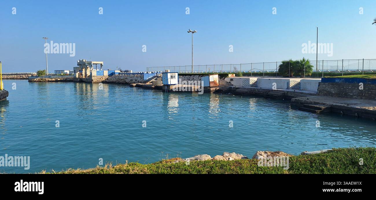 Ein ruhiger Blick auf einen Hafen mit angedockten Fähren und Booten unter einem klaren blauen Himmel. Das ruhige Wasser reflektiert die umgebenden Strukturen und Gefäße auf einem Stockfoto