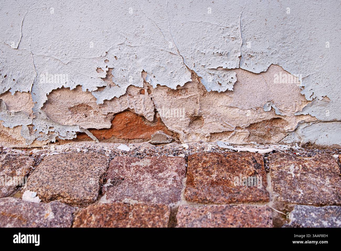 Verwitterte Wand mit gerissener und abblätternder Farbe, die den Putz verschlechtert und alte Ziegelsteine freilegt, die Verfall und Alterung symbolisieren. Kopierbereich Stockfoto