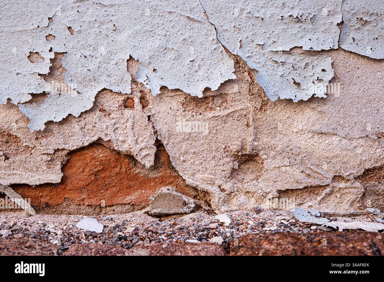 Verwitterte Wand mit gerissener und abblätternder Farbe, die den Putz verschlechtert und alte Ziegelsteine freilegt, die Verfall und Alterung symbolisieren. Kopierbereich Stockfoto