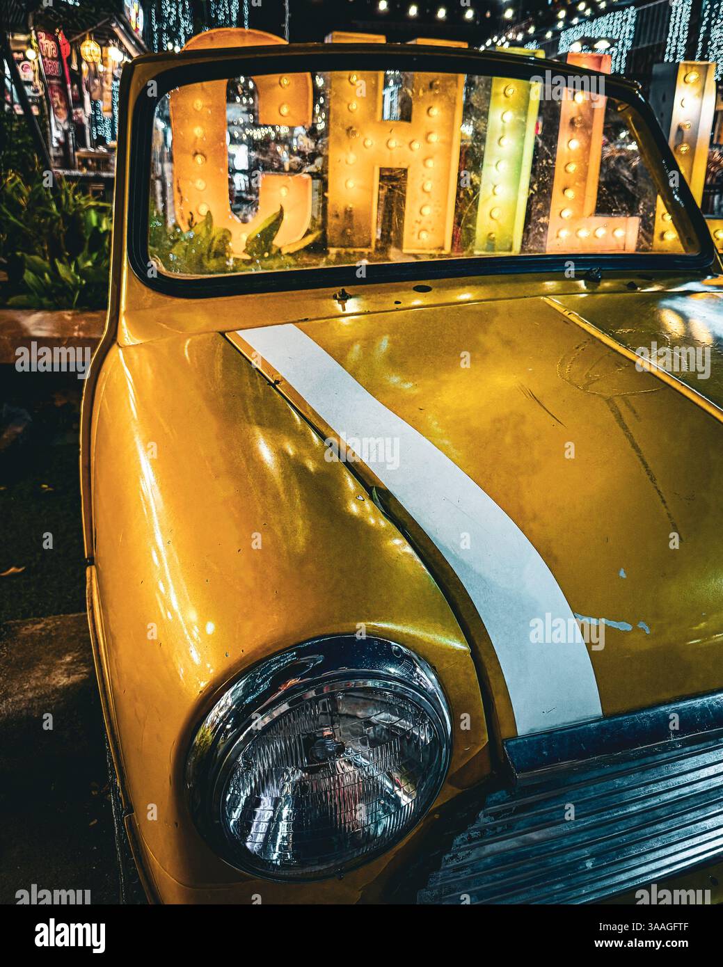 Gelbes Oldtimer bei Nacht – Retro Chill Vibes Eine Nahaufnahme eines gelben Oldtimers, der nachts in einer lebhaften, beleuchteten Umgebung geparkt wurde. Stockfoto