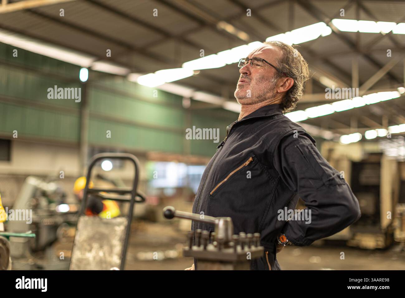 Ältere Arbeiter müde erschöpfte Muskelschmerzen, leiden unter Schmerzen im unteren Rückenbereich durch harte Arbeit in einer Fabrik für Schwerindustrie. Stockfoto